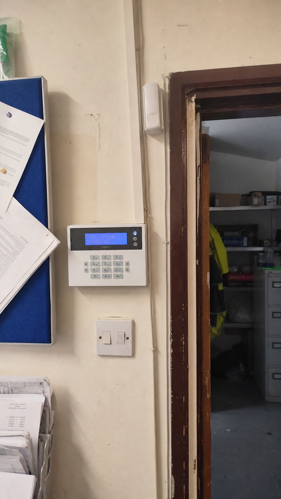 Phone-style photo of a commercial intruder alarm keypad beside a staff door